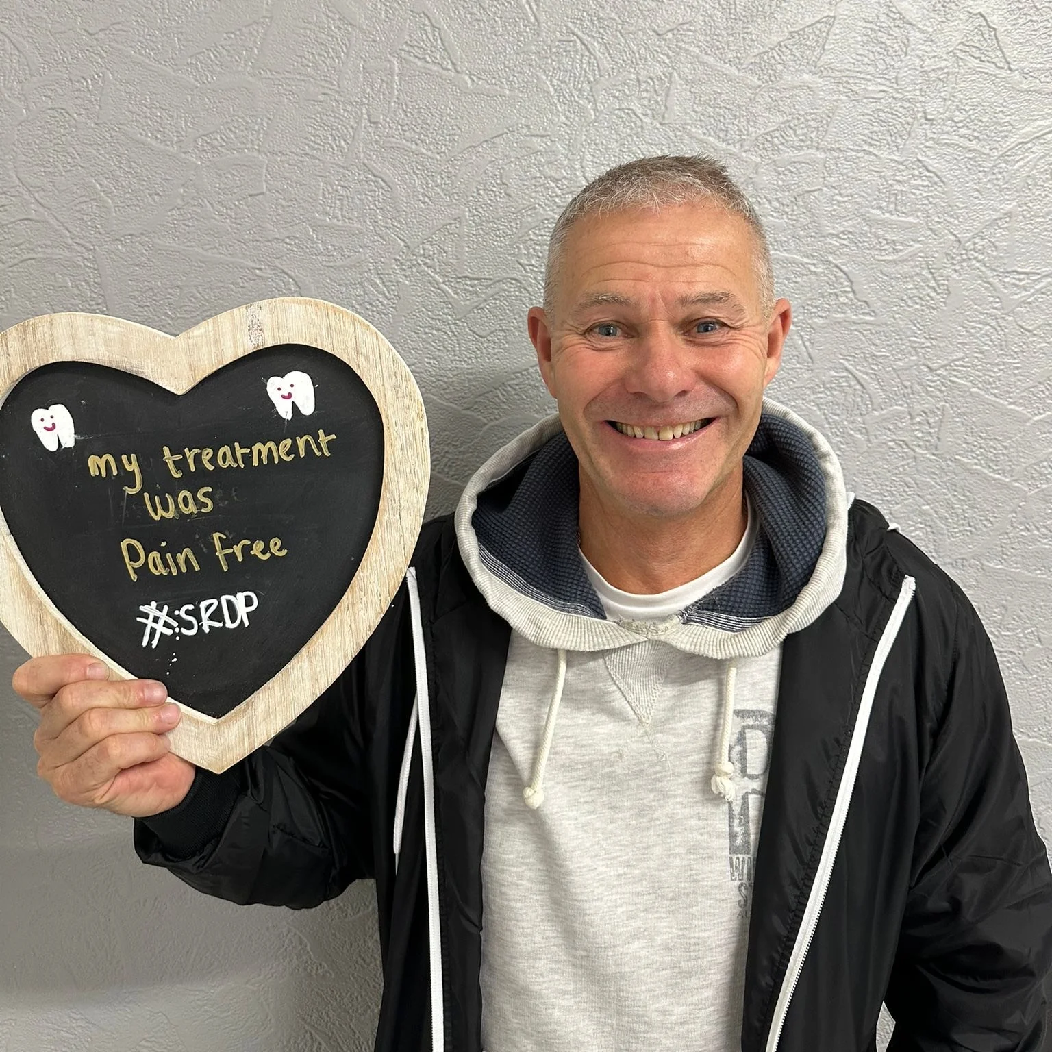 A patient holding a heart-shaped board reading "my treatment was pain free"